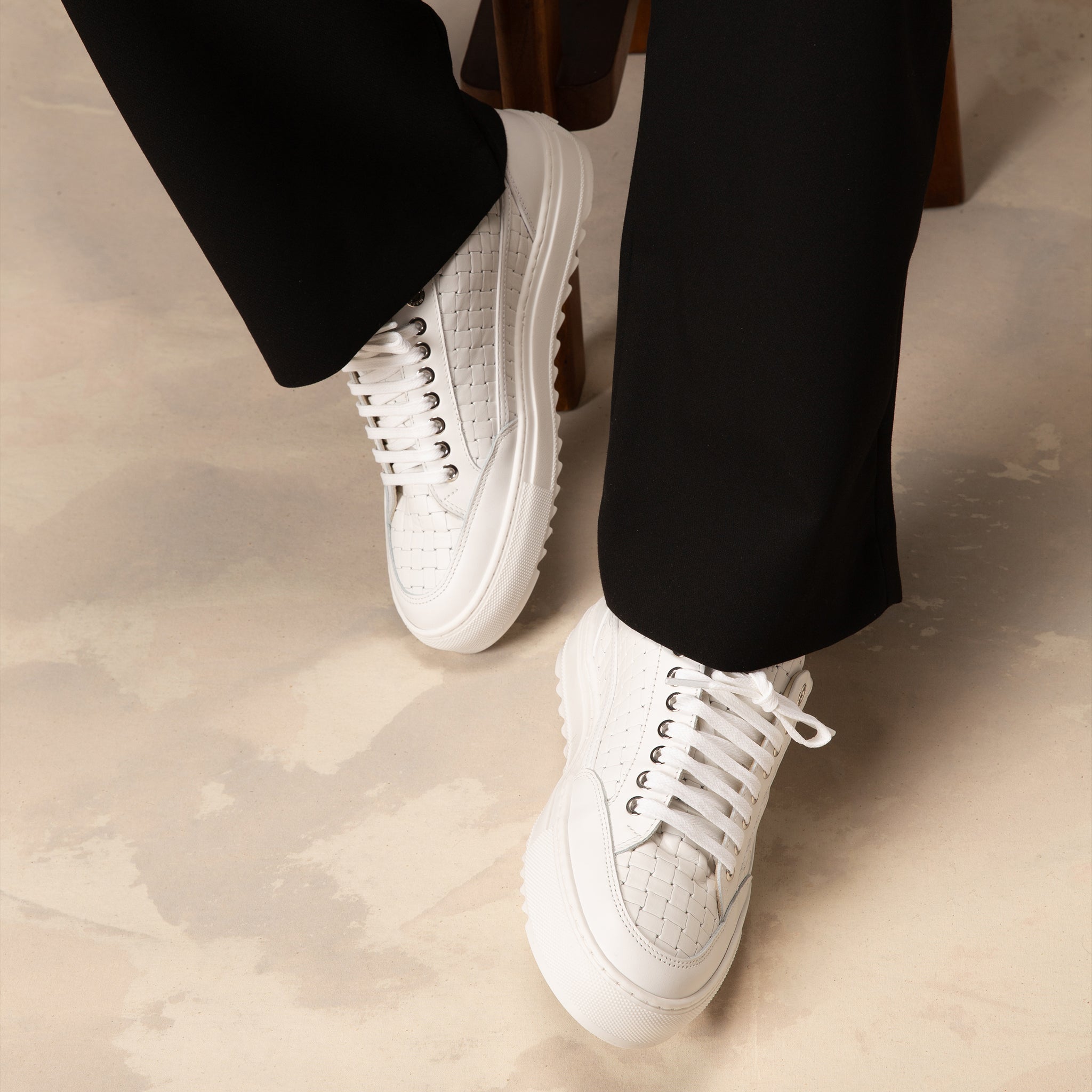 White sneakers worn with black pants on a light-colored floor.