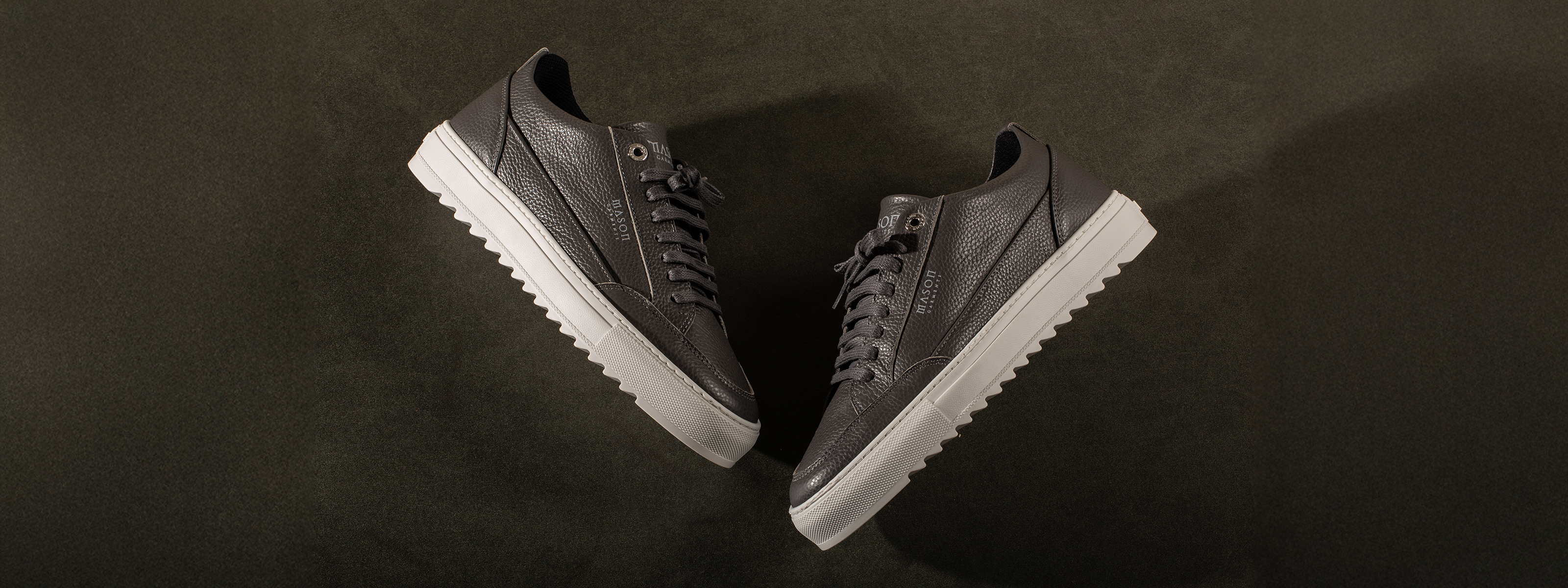 Pair of dark gray sneakers with white soles on a dark background