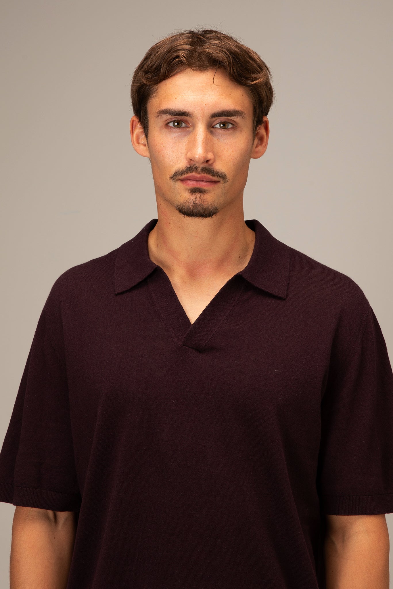 Man wearing a dark brown polo shirt against a plain background