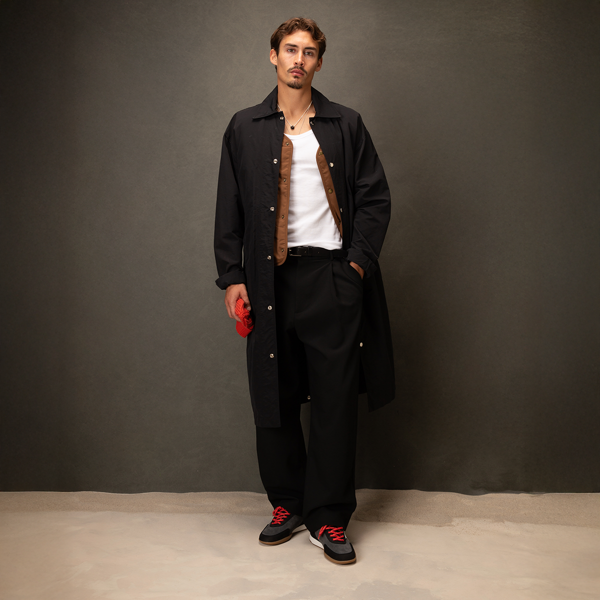 Man wearing a black coat and pants with red accents against a gray background