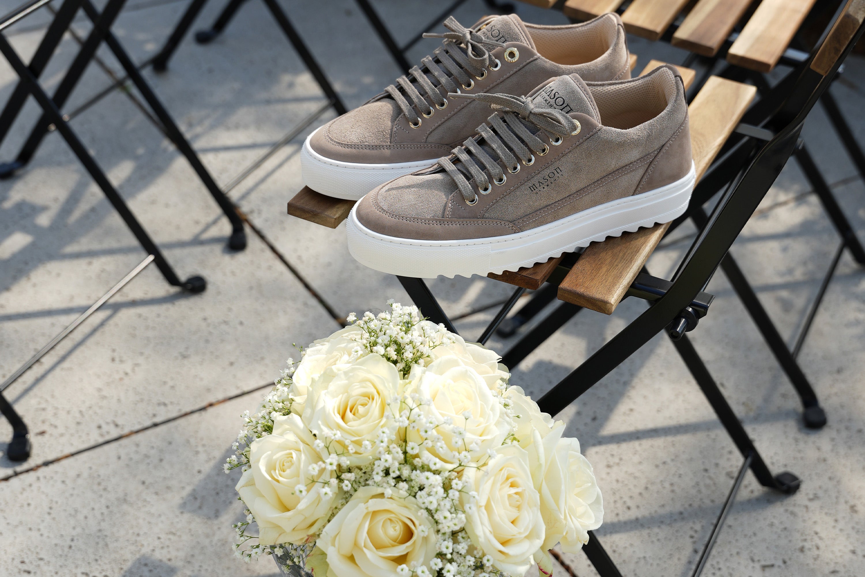 Pair of brown sneakers on a chair with a bouquet of white flowers in the foreground.