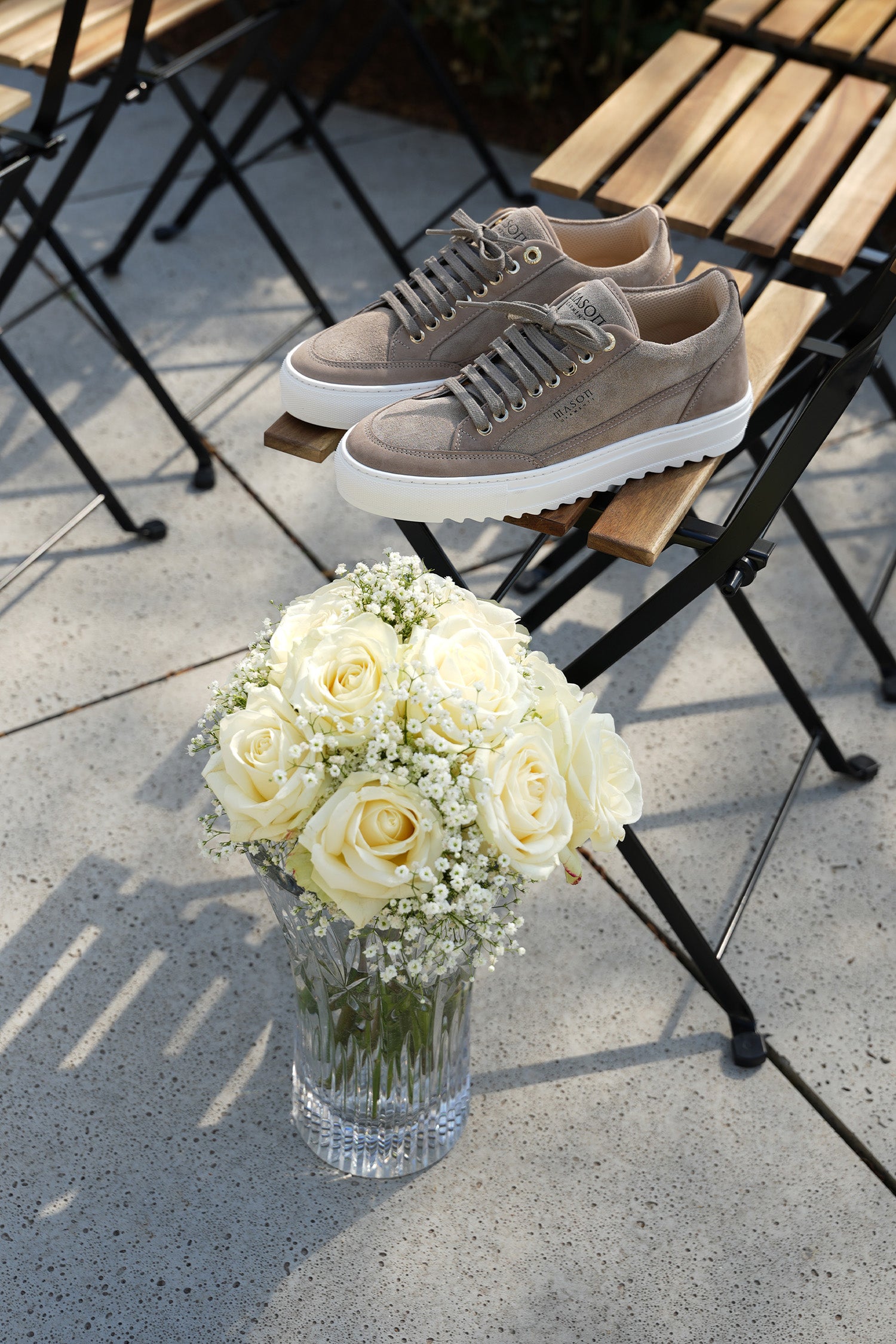 Pair of beige sneakers on a chair with a vase of white flowers on a concrete surface at the wedding