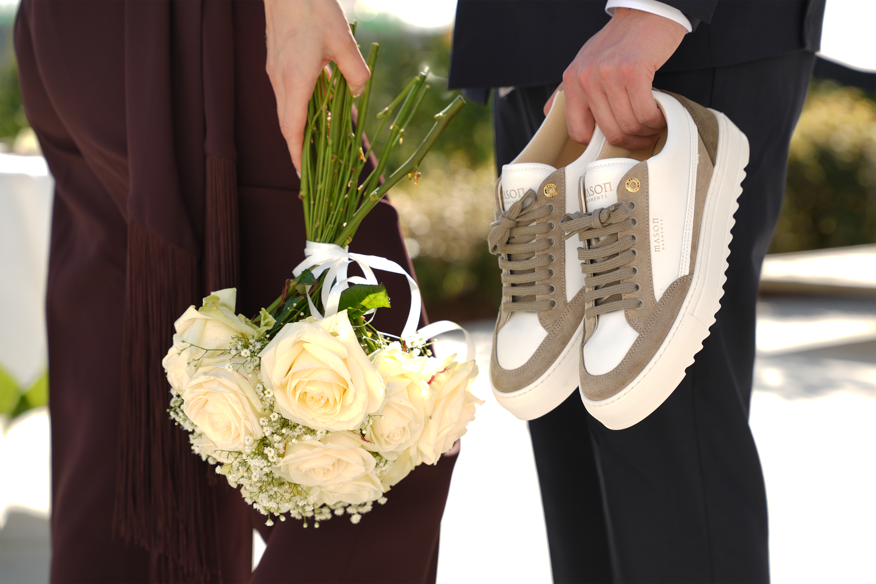 Person holding a bouquet of flowers and another person holding sneakers outdoors in the wedding setting