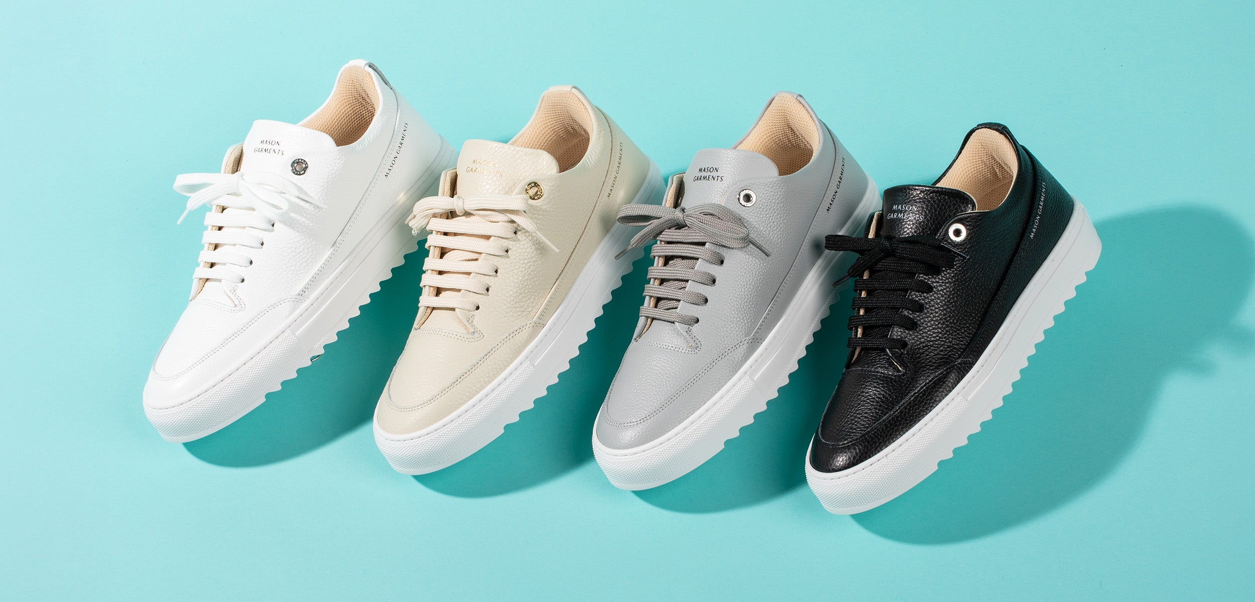 Four pairs of sneakers in white, beige, gray, and black on a light blue background
