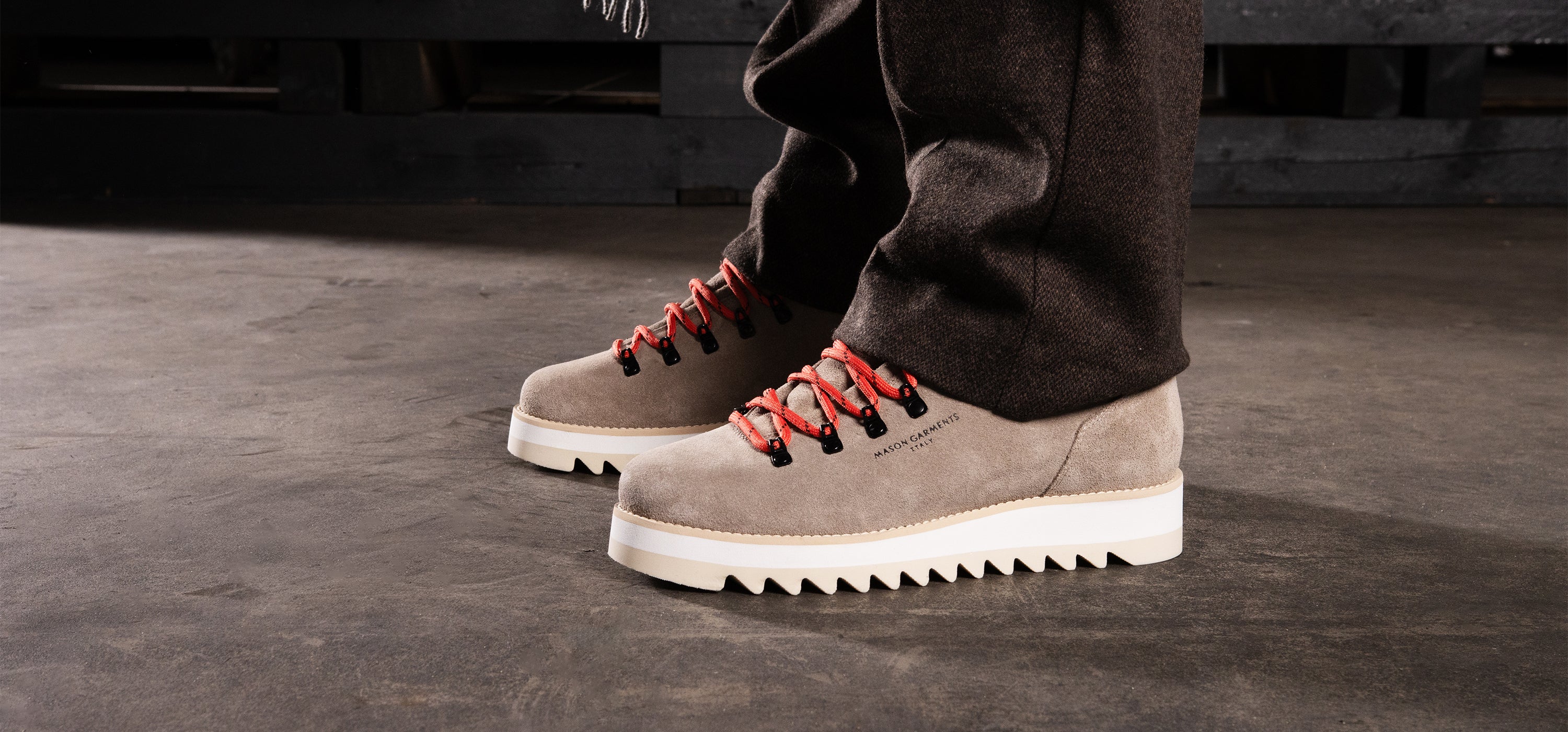Brown suede boots with red laces worn by a person on a dark concrete floor.
