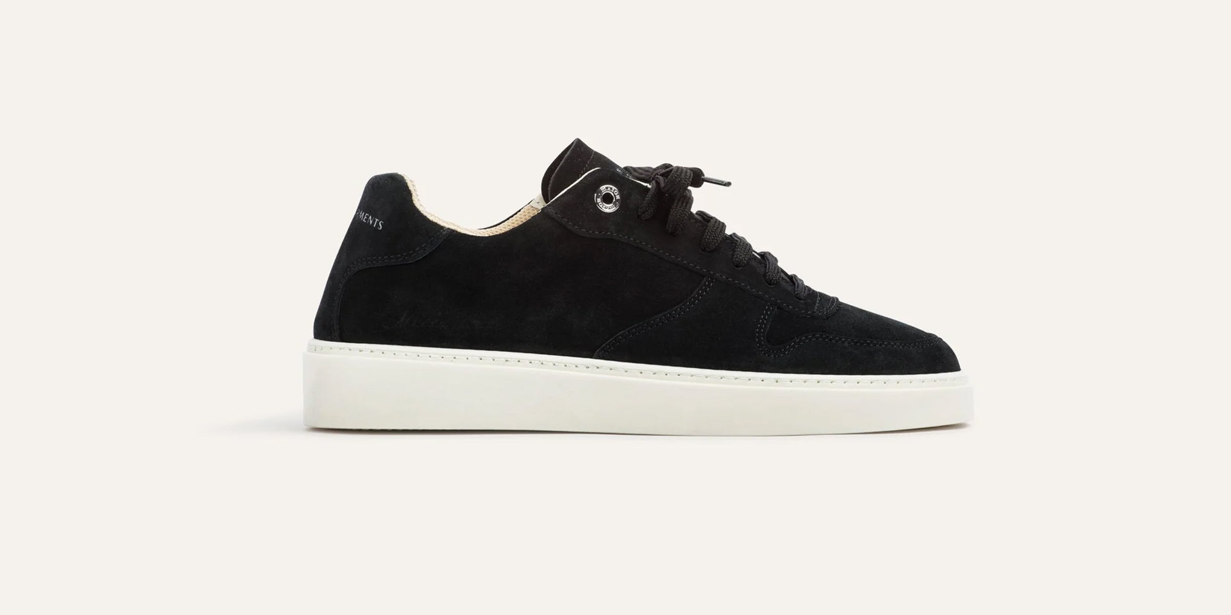 Black suede sneaker on a light beige background